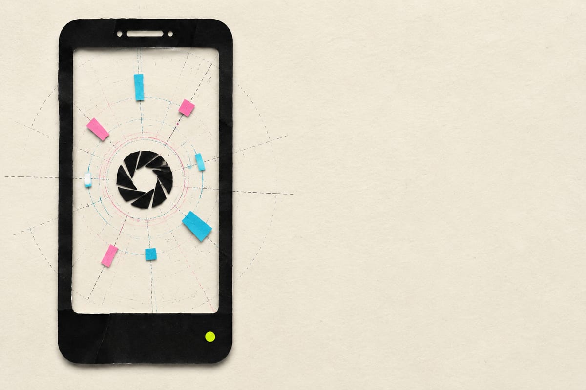 A paper-cut phone with a closed shutter aperture on its screen, ringed by cyan and pink fragments